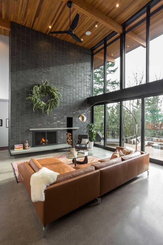 a mid-century modern living room with a glazed wall, a black brick fireplace, amber leather seating furniture, a glass coffee table