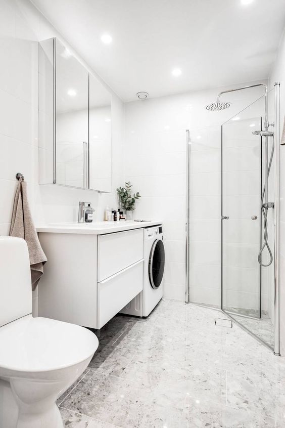 a neutral minimalist bathroom with a shower in the corner, a floating vanity, a washing machine, a grey terrazzo floor and a mirror cabinet