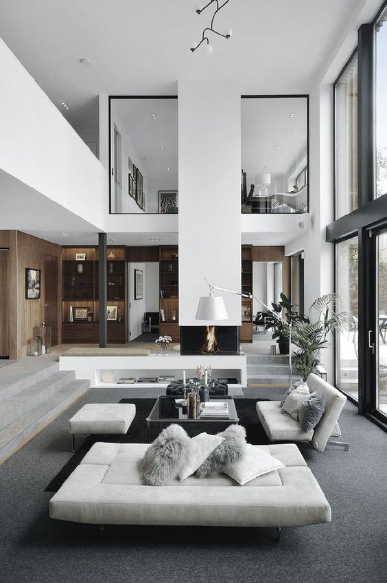 a minimalist double-height living room with a glazed wall, a fireplace, grey seating furniture, a glass coffee table and a floor lamp