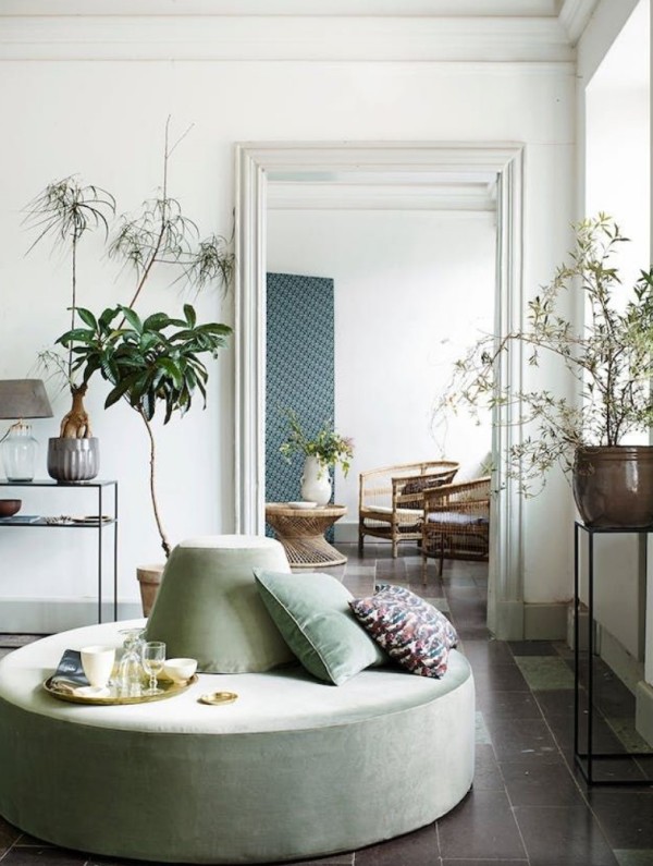 a beautiful space with large round sage green ottoman and potted plants is a very relaxed and airy space
