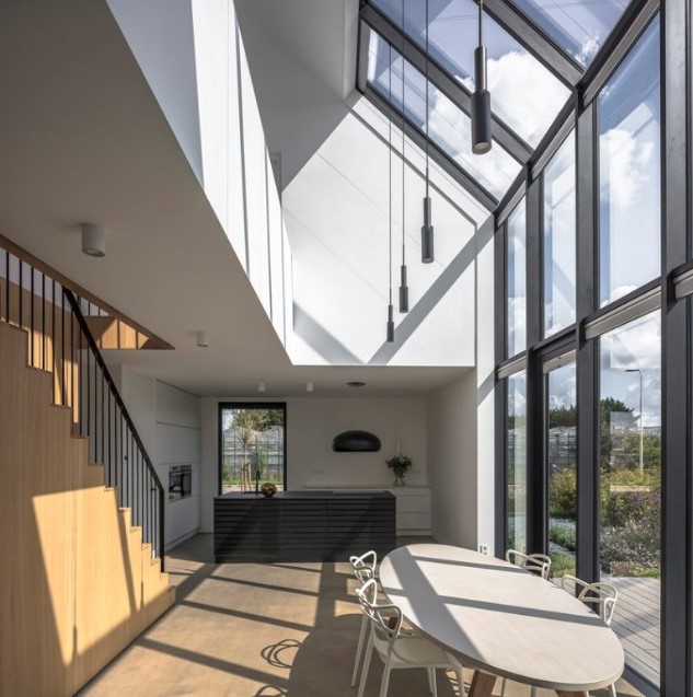 a minimalist kitchen and dining space by the glazed wall with a skylight and pendant lamps that highlight the height of the ceiling