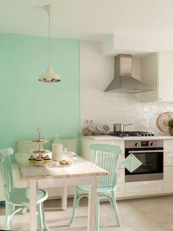 a mint green and white kitchen with a mint accent wall and chairs, neutral shaker cabinets and a glossy tile backsplash, a neutral table