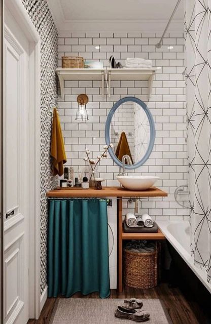 a small and pretty bathroom clad with white subway tiles, with a black bathtub, a woodne vanity with a washing machine and an oval mirror