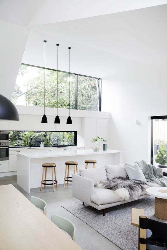 a minimalist open layout with a clerestory window and a window backsplash, a white kitchen, a cozy sitting space and wooden tables