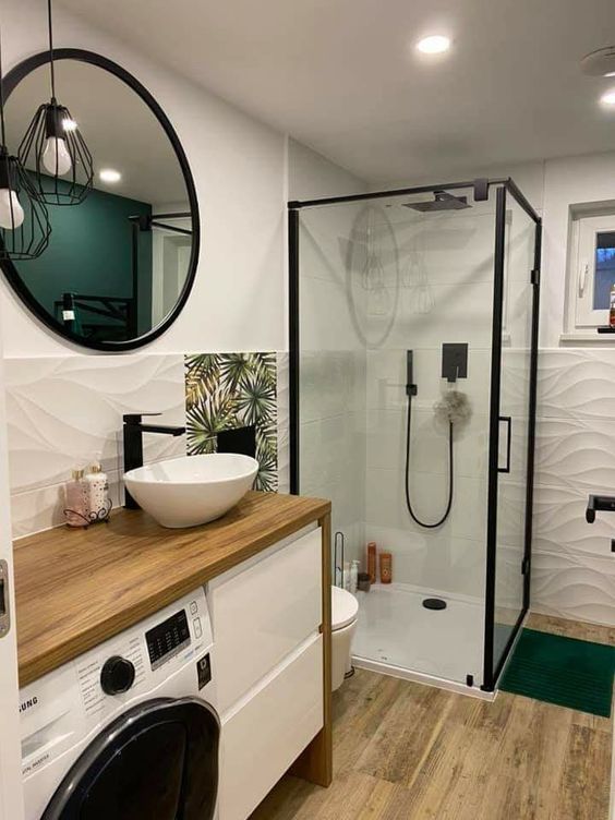 a small modern bathroom with a vanity and a built-in washing machine, a glass-enclosed shower, white textural tiles and a wooden floor