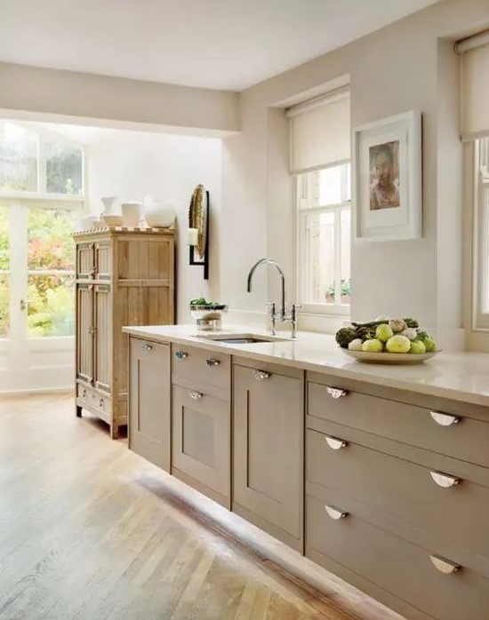 a lovely taupe kitchen with shaker cabinets, vintage knobs, white stone countertops and a vintage rustic cupboard for storage