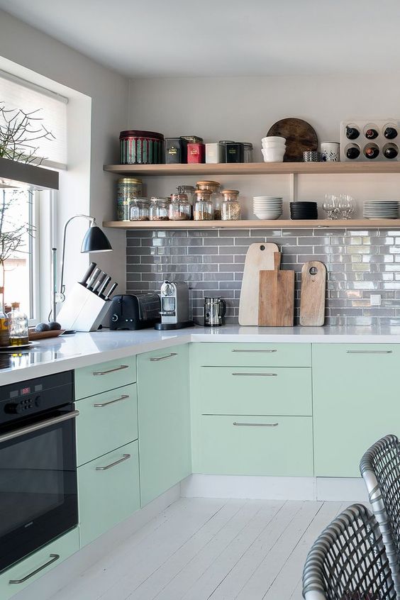 a mint green Scandinavian kitchen with grey tiles, white stone cabinets, open shelves, black lamps is a very cool space