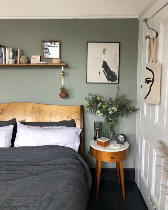 a modern bedroom with a sage green accent wall, a stained bed and a small nightstand, an open shelf, some contrastign artwork