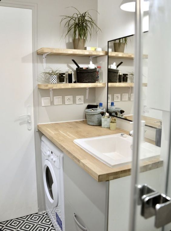 a small neutral bathroom with a vanity and a built-in washing machine, a shower space, open shelves and a mirror in a black frame