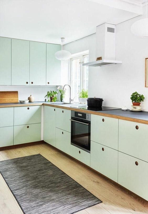 a mint green Scandinavian kitchen with MDF cabinets, black countertops and a white backsplash, a dark rug and built-in appliances