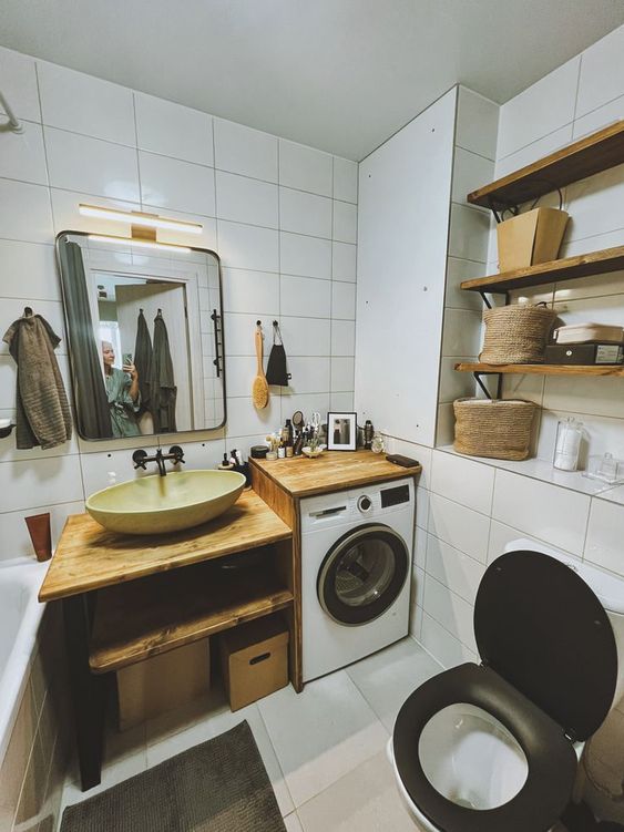 a small white bathroom clad with white tiles, with wooden shelves and an open timber vanity plus a built-in washing machine