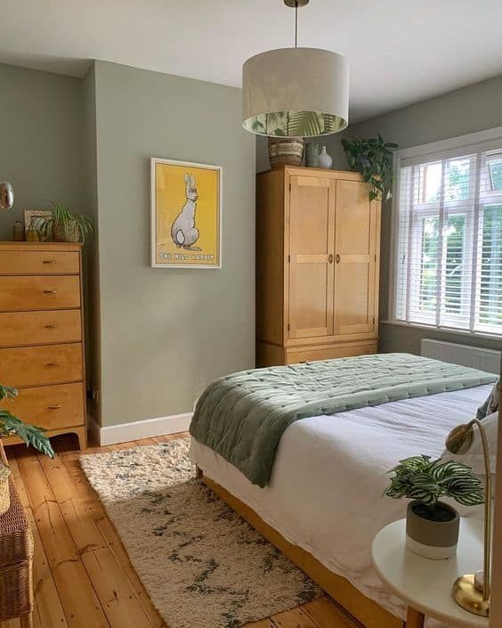 a sage green bedroom with stained furniture, neutral and green bedding, a printed rug and a printed pendant lamp