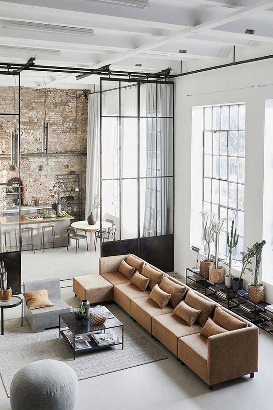 a stylish modern living room with double-height windows, a rust sofa, side tables and a grey chair, a console table with plants and books