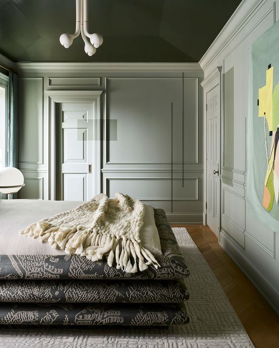 a sage green contemporary bedroom with a dark green ceiling, a bed of stacked mattresses, a cool chandelier and a bold artwork