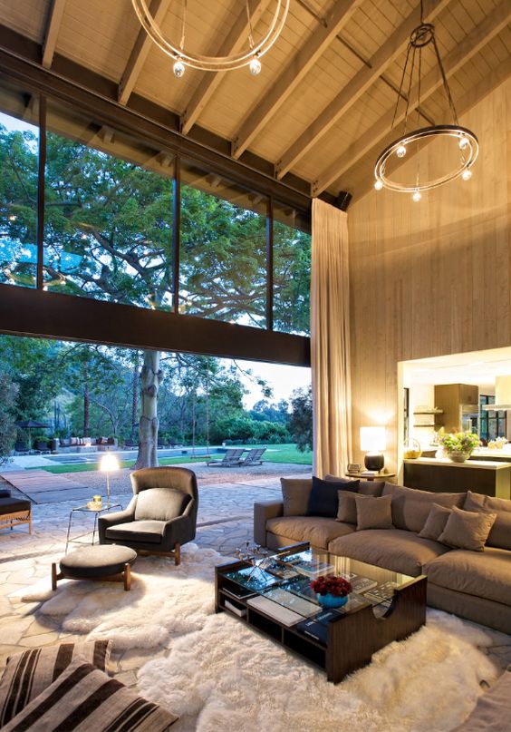 a welcoming living room with a glazed wall, grey and taupe seating furniture, round chandeliers and a coffee table