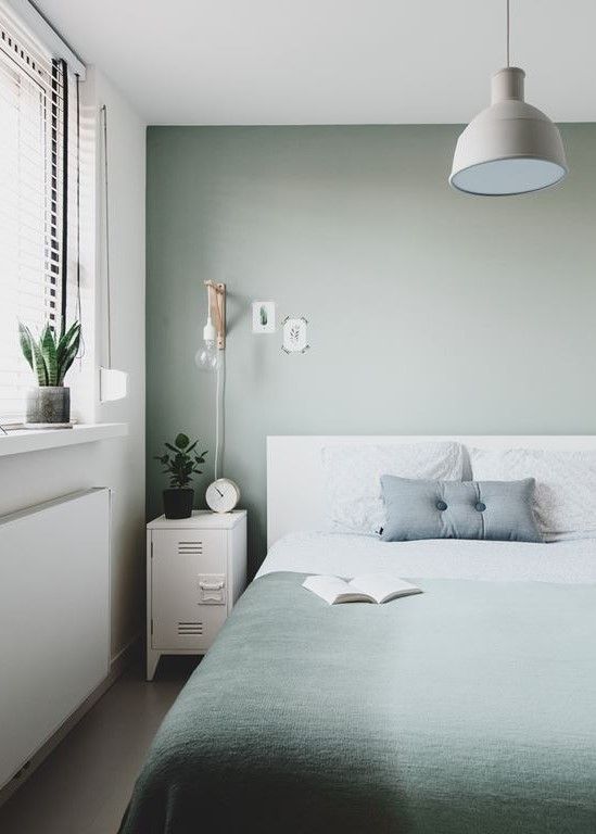 a Scandinavian bedroom with a white bed and green and white bedding, white metal cabinets, a pendant lamp and sconces