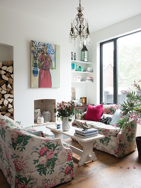 a chic living room with a non-working fireplace, floral sofas, a bench as a coffee table, a crystal chandelier