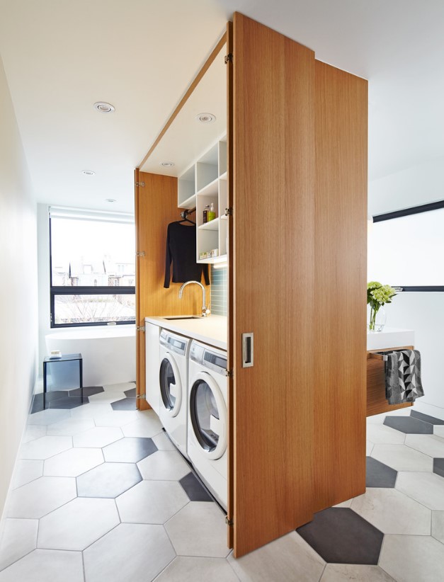 a modern bathroom clad with black and white hexagon tiles, with a large storage cabinet that hides a washing machine, a dryer and a sink