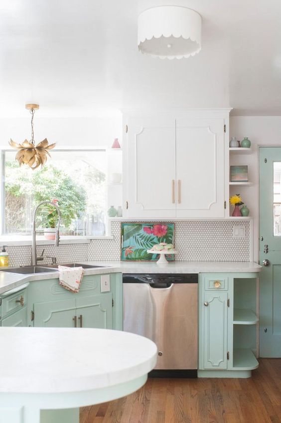 a retro kitchen done in white and mint, with elegant cabinets, white stone countertops, a white penny tile backsplash and gold fixtures