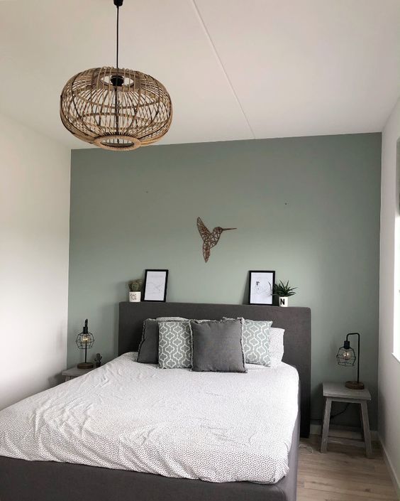 a small bedroom with a sage green accent wall, a dark upholstered bed, printed bedding, small nightstands and a wooden pendant lamp