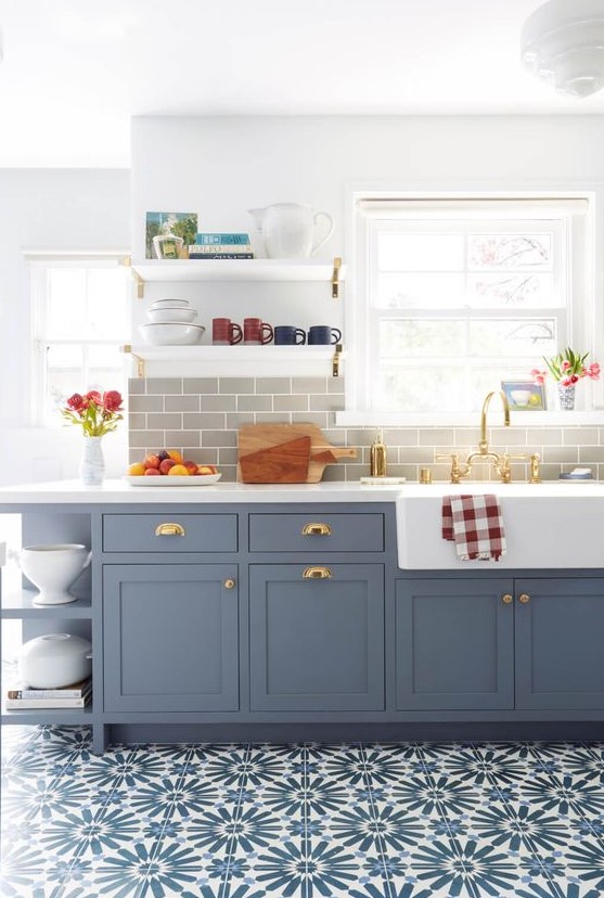 a beautiful blue shaker style kitchen with a grey subway tile backsplash, white quartz countertops and touches of brass