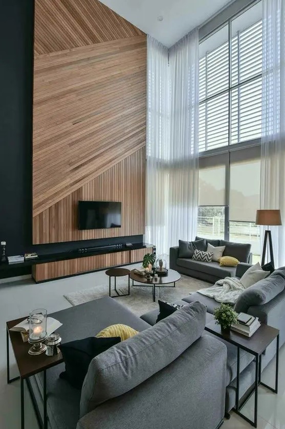 a contemporary double-height living room in the shades of grey, with an accent wood slat wall, a TV and a TV unit, double-height windows that bring a lot of light