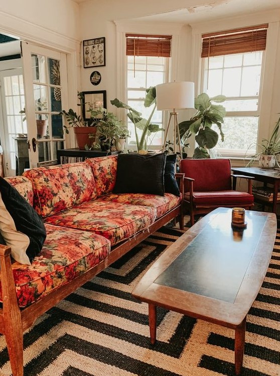 a mid-century modern lviing room with a black and white rug, a floral sofa, rust-colored chairs, potted plants and a floor lamp