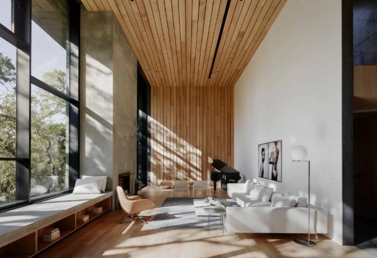 a contemporary double-height living room with a large window and a windowsill bench, a white corner sofa, a coffee table and a textural slat accent wall and ceiling
