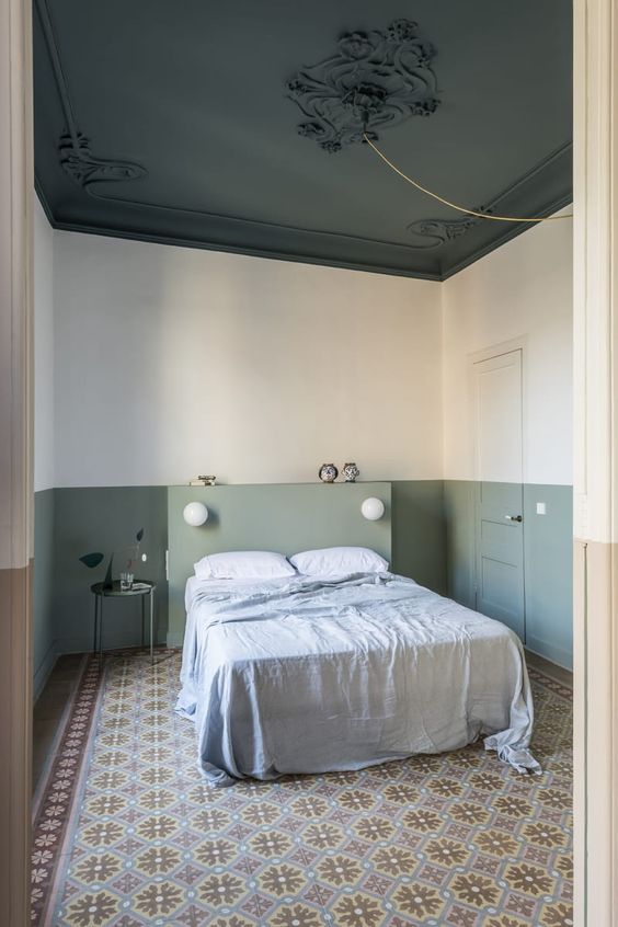 a sophisticated bedroom with color block sage green walls, a bed with a sage green headboard, a printed rug and a dark green ceiling