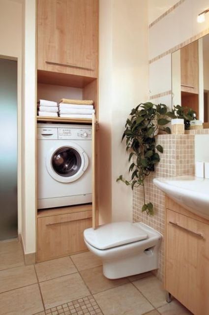 a neutral-colored bathroom with small and large tiles, a built-in storage unit that hides a washing machine and a wooden vanity