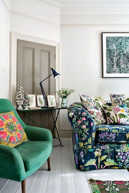 a neutral living room with a moody sofa, an emerald chair, a console table and moody floral artwork