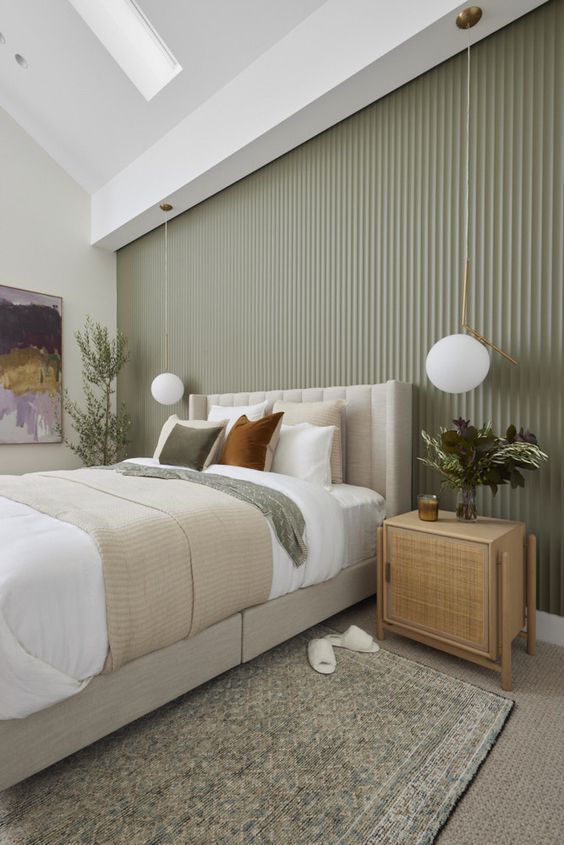 a stylish modern bedroom with a sage green fluted accent wall, a neutral upholstered bed with neutral bedding, rattan nightstands and pendant lamps