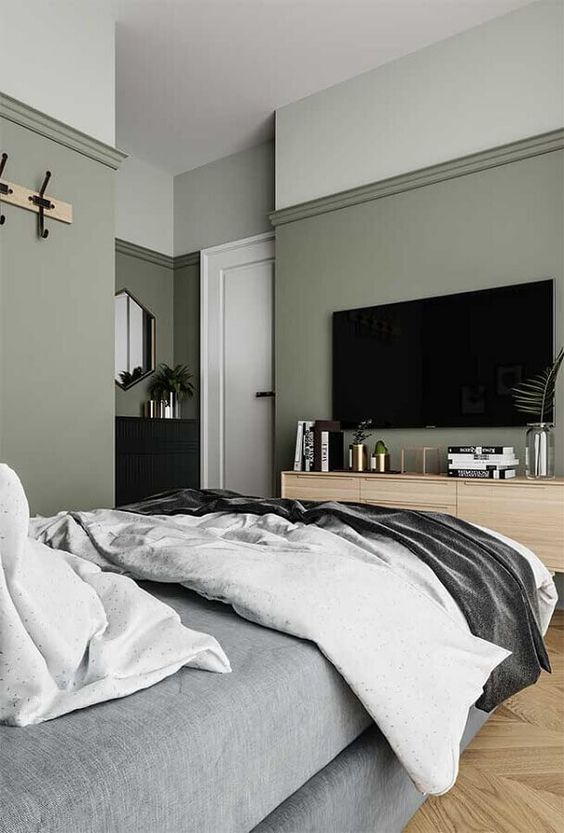 a stylish modern bedroom with sage green walls, an upholstered grey bed with grey bedding, a stained dresser and a black one