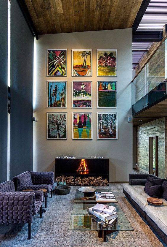 a bold and catchy living room with a grid gallery wall over the fireplace, purple chairs, glass coffee tables and a neutral sofa