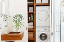25 a white bathroom with a glass-enclosed shower space, a large storage unit, a washing machine and a dryer and shelves for storage, a wooden sink