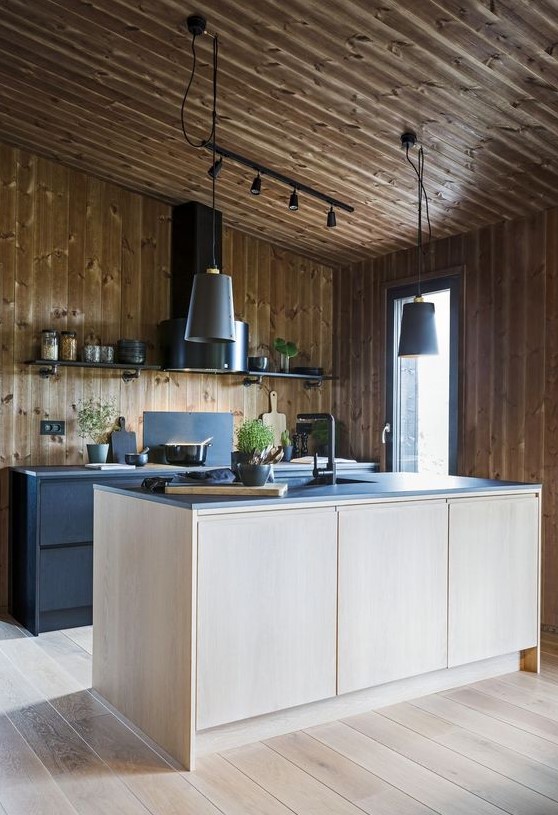 a contemporary chalet kitchen all clad with wood, with black metal cabinets and a plywood kitchen island, black countertops and a black hood