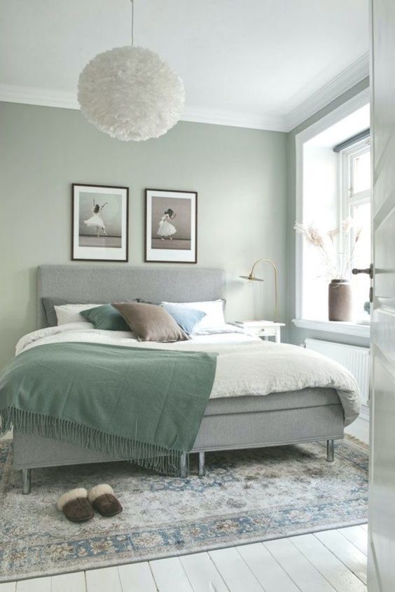 an airy Scandinavian bedroom with sage green walls, a grey upholstered bed with green and neutral bedding, a printed rug