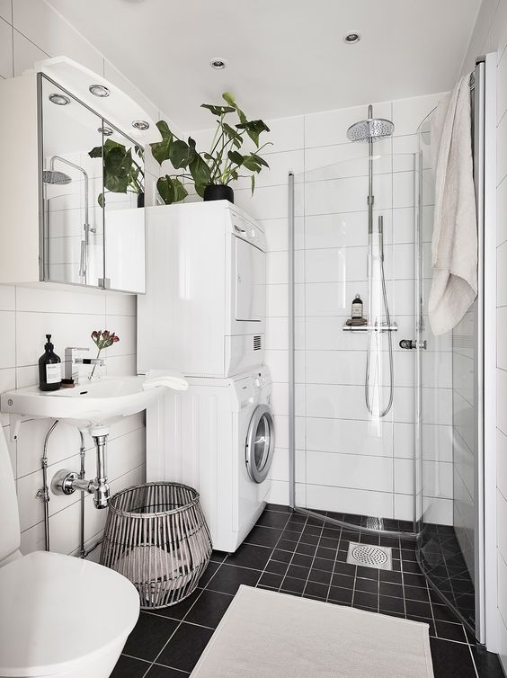 a black and white Scandinavian bathroom with white and black tiles, a shower in the corner, a washing machine and a dryer and a sink