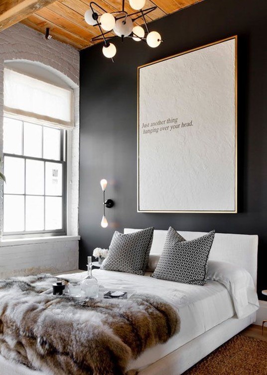 a double-height bedroom with a black accent wall and an oversized artwork, a white upholstered bed with printed bedding, a chandelier and sconces