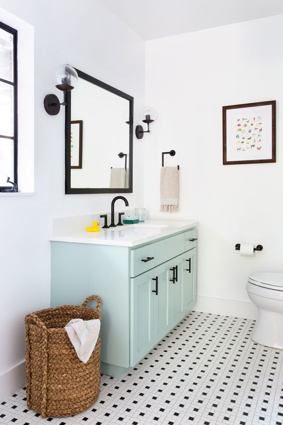 a black and white bathroom clad with tiles on the floor, a mint vanity, black fixtures and a black mirror frame