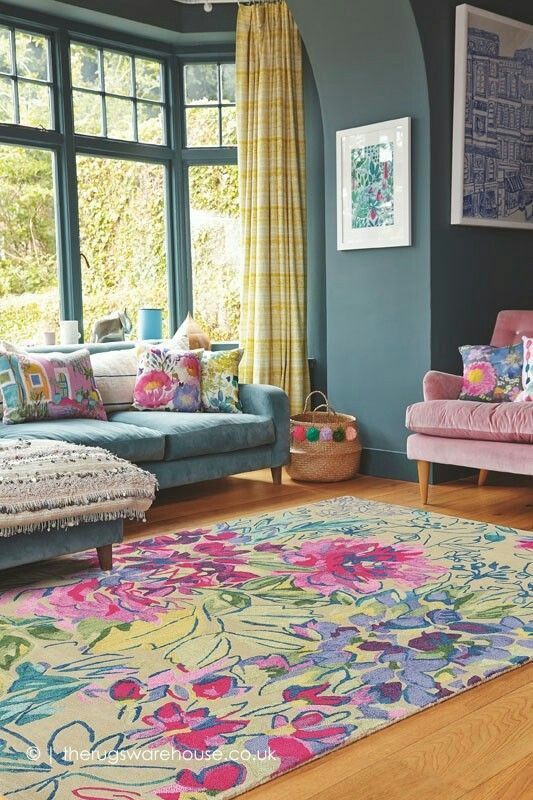 a bold living room with slate blue walls, a blue sofa and colroful pillows, a pink chair, a bright floral rug