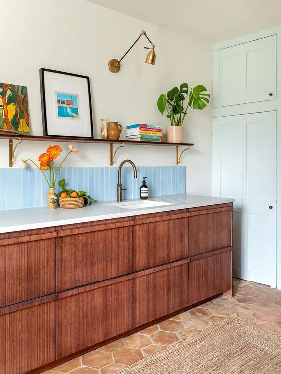 a cool and chic mid-century modern kitchen with stained cabinets, white stone countertops, an open shelf, artwork and books and potted plants