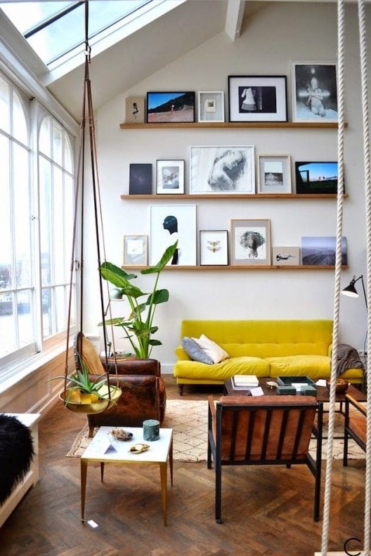 a double-height living room with a ledge gallery wall, a mustard sofa, leather chairs, coffee tables and potted plants