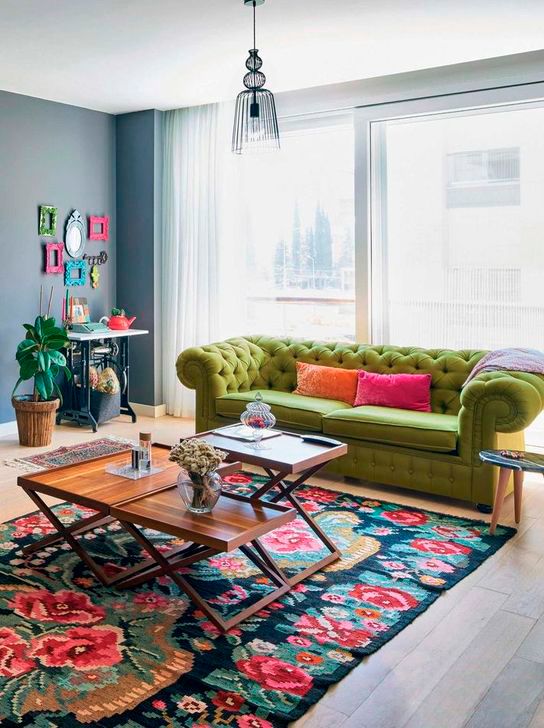 a bright living room with a console table and a colorful frame gallery wall, a green sofa, a bright floral rug and coffee tables