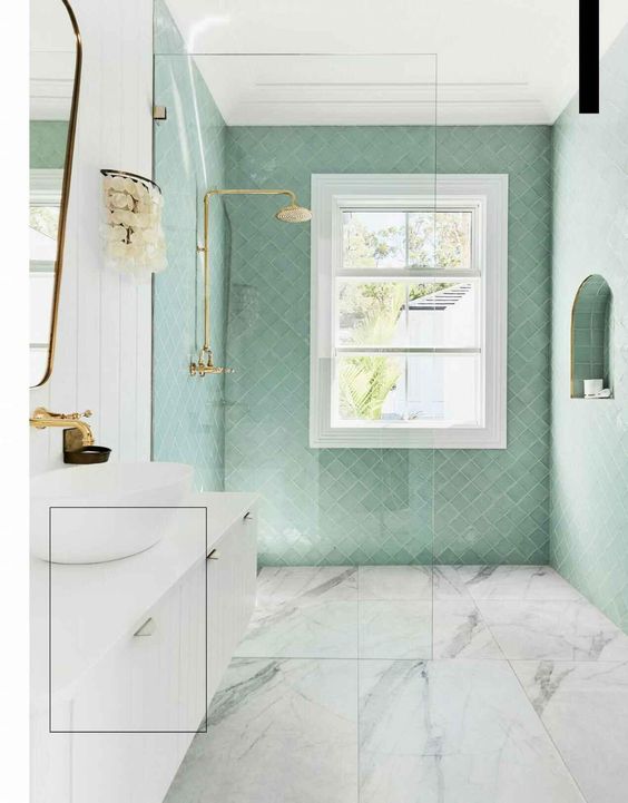 a chic bathroom clad with mint herringbone tiles and marbles ones, a white floating vanity, gold fixtures and natural light