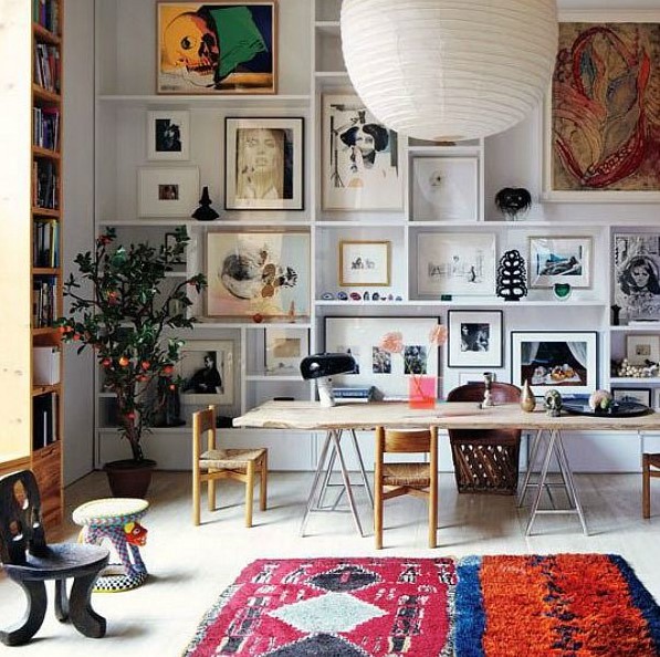 a double-height space with a large gallery wall taking the whole wall, a bookcase, a living edge desk, several chairs and a bright rug