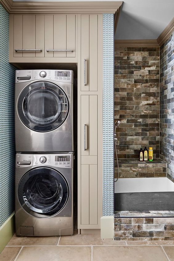 a modern bathroom with a shower space clad with brown stone-like tiles, with a stacked washine machine and a dryer