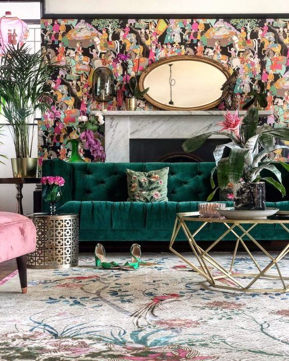 a bright living room with a whimsical wallpaper accent wall and a fireplace an emerald sofa, a pink chair, a gold base coffee table and a floral rug