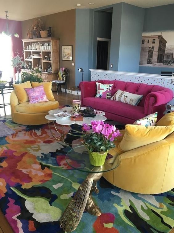 a colorful living room with a fuchsia sofa and yellow chairs, a super bold floral print rug and mismatching coffee tables