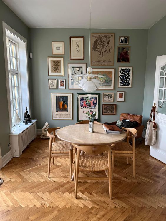 a sage green dining room with a wooden table, rattan chairs, a bright gallery wall and some lovely decor